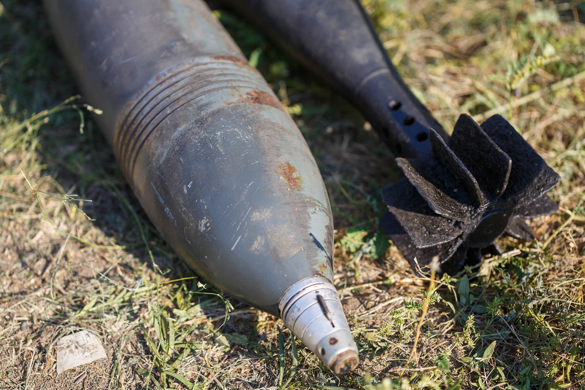 Nahaufnahme einer alten, rostigen Fliegerbombe, die auf einer Wiese liegt. Die Bombe zeigt deutliche Gebrauchsspuren und wird vermutlich für eine kontrollierte Entschärfung vorbereitet.