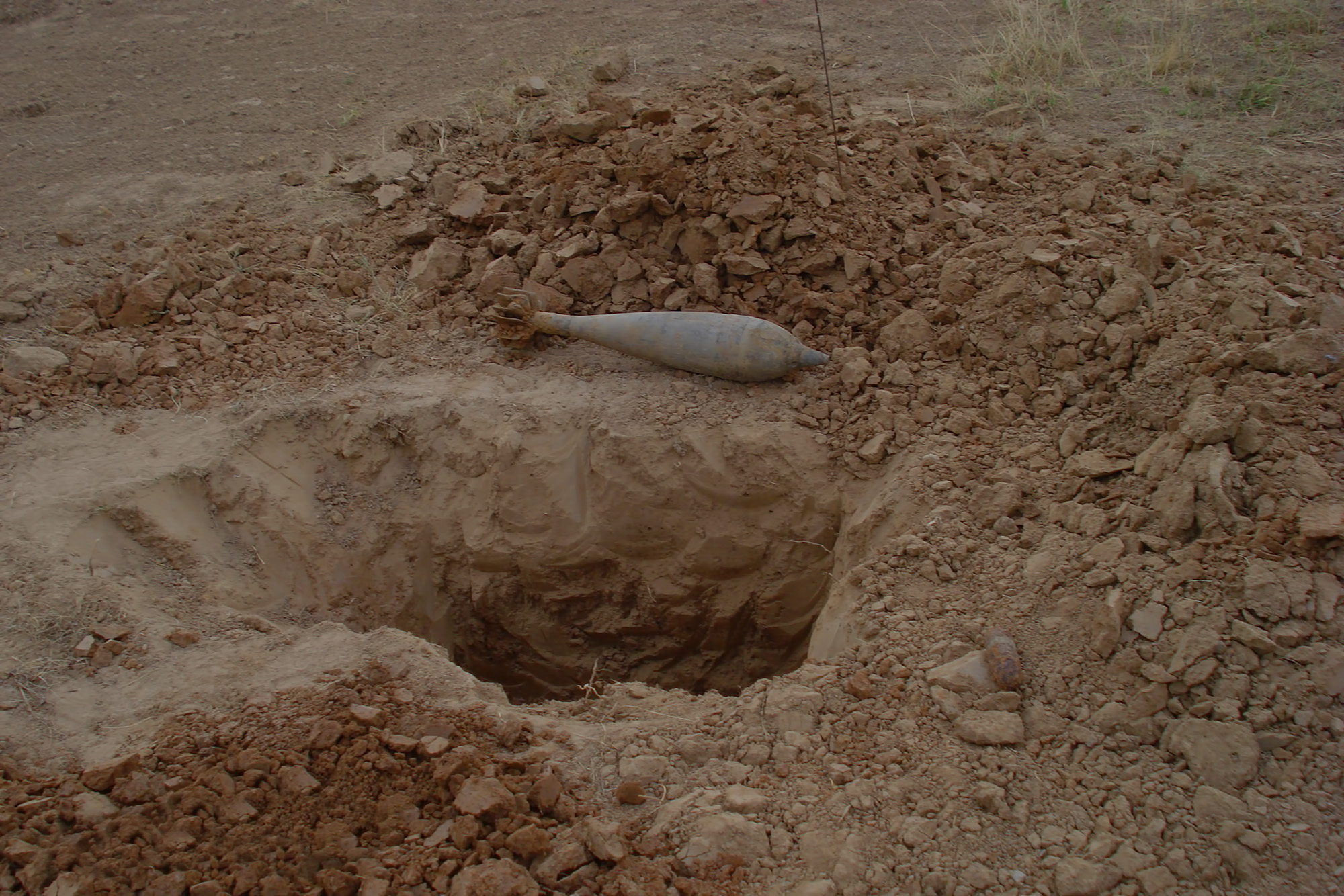 Teilweise freigelegte alte Fliegerbombe liegt in einer ausgehobenen Erdgrube. Die Szene zeigt eine kontrollierte Bergung auf einem sandigen Baustellengelände.