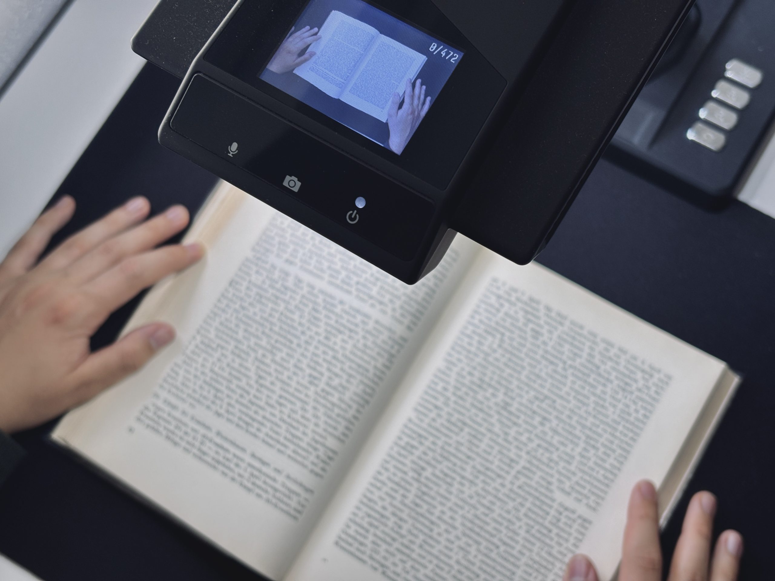 Person scannt ein aufgeschlagenes Buch zur historischen Recherche der Lufbildauswertung mit einem Dokumentenscanner. Auf dem Display des Geräts ist die Buchseite mit den Händen des Nutzers zu sehen.